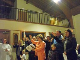 People raising hands in a church choir or service, with a balcony and wooden interior visible