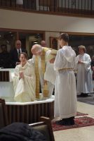 Priest in white vestments blessing a woman in a church during a religious ceremony