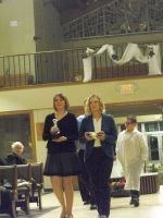Two women walking down an aisle in a decorated indoor venue, one in a dark skirt suit and one in a navy suit.