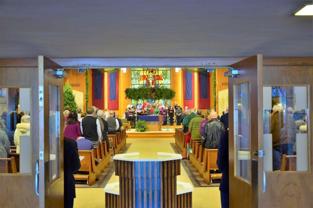 Church sanctuary with people seated in pews facing a decorated altar and colorful banners