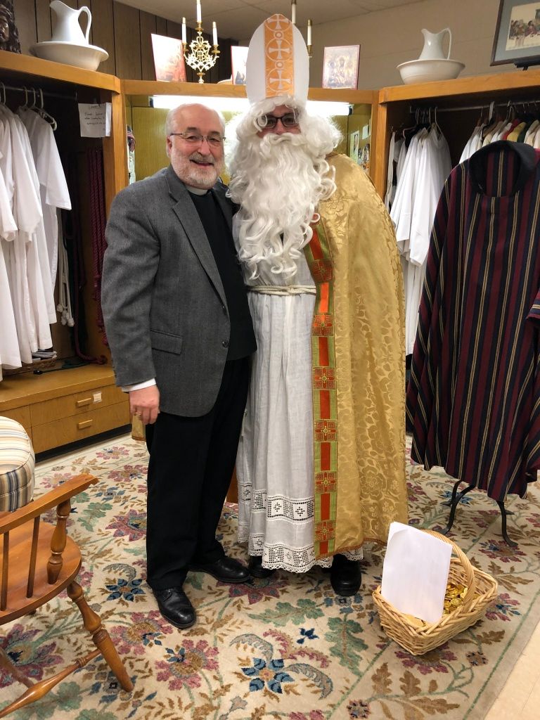 Two men standing together in a clothing boutique, one wearing a white robe and gold cape, the other in a gray jacket.