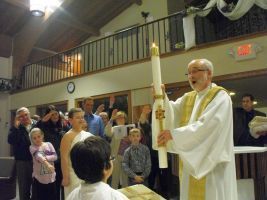 Priest holding a tall candle during a church ceremony, with congregants standing nearby.