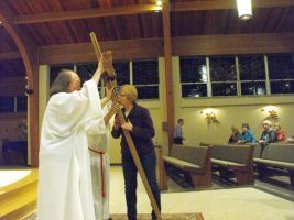 Two people hold long wooden staffs in a church-like hall during a ceremony.