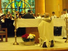Priest kneeling at altar during church service, with choir and stained glass in the background