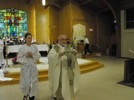 Two people in white robes walk through a church aisle during a religious ceremony.