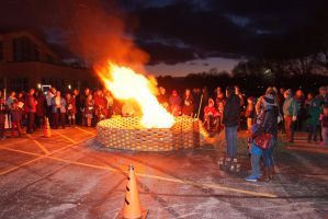 Crowd gathered around a large bonfire at night in an outdoor plaza