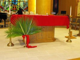 Church altar with red cloth, palm frond decoration, and gold candlesticks on a tiled floor.