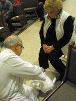 Two people in a seating area, one kneeling and adjusting the other's foot or shoe.