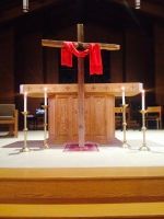 Wooden cross draped with red cloth before a church altar and candles
