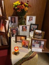 Memorial display with framed photos, flowers, candles, and notes arranged indoors on a table