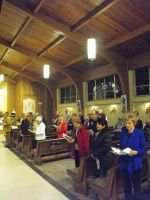 People gathered inside a wooden church, standing and seated in prayer or reflection.