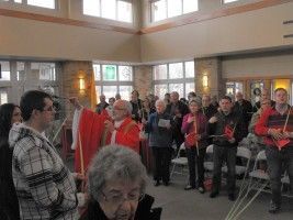 People gathered indoors in a bright hall, some wearing red and black, listening to a speaker.