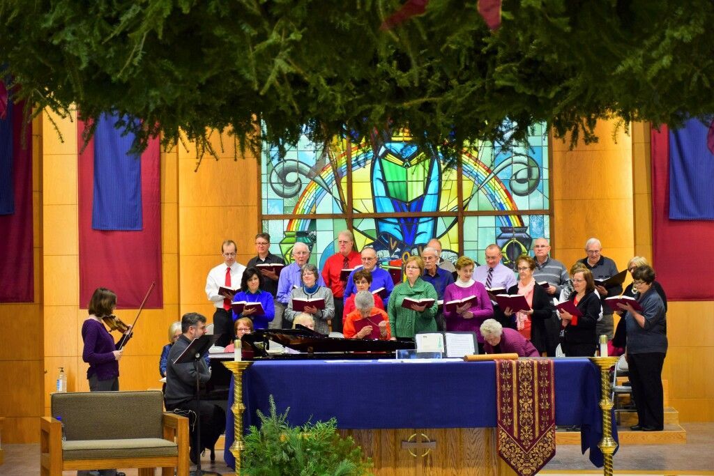 Choir singing in a church sanctuary before a stained-glass window and altar table