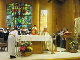 Church altar service with choir, stained-glass window, and priest at the altar