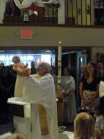 Priest in white robe holding up a chalice during a church service, congregation standing nearby