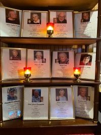 Memorial display with framed photos and messages on shelves, lit by small red candles.
