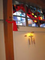 Stained-glass church window above a beige wall with a lit wall sconce and a red ribbon decoration