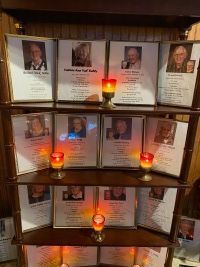 Memorial shelf with framed photos and lit candles honoring several people