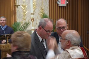 People conversing in a church hall, with a man in a suit speaking to an older man at a reception.