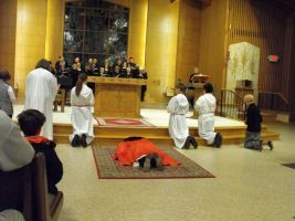 People kneel before an altar in a church, with one person prostrate on a red rug.