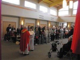 People gathered indoors for a ceremony, with clergy in red and white robes at the front.