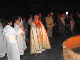 Clergy in white and gold robes lead a nighttime candlelight procession outdoors