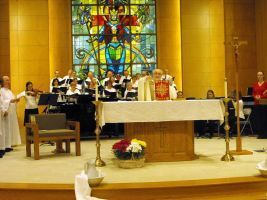 Church altar during a service, with clergy and musicians before a stained-glass window.