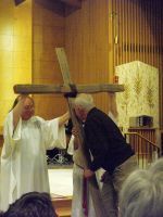 Priest and assistant carrying a large wooden cross inside a church during a service
