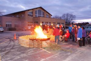 People gathered around a bonfire outside a brick building at dusk