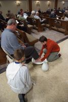 Child tying shoe for seated person in church pews during a gathering