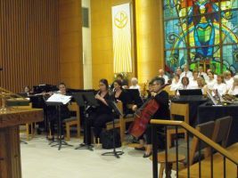 Musicians performing in a church sanctuary with stained glass and wooden pews.
