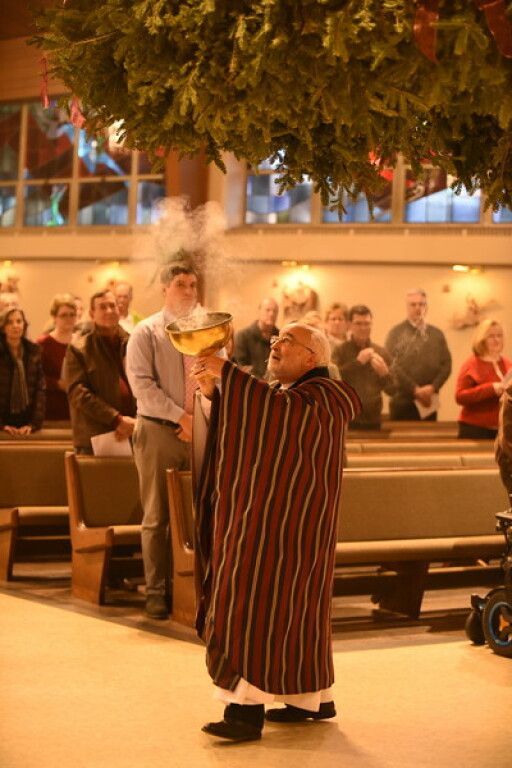 Person in striped robe and head covering carrying a lit candle during an indoor religious procession