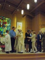 Church ceremony with people on stage, stained glass, and a priest blessing a couple