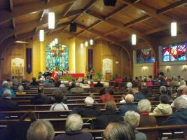 Church congregation seated in pews facing the altar and stained-glass windows