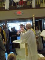Priest in white vestments leads a church service before a crowd near the altar.