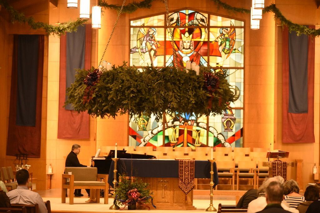 Church interior with a large hanging greenery centerpiece above the altar and stained-glass window behind it