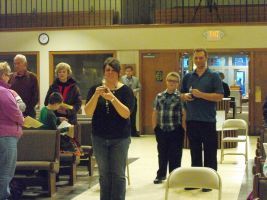 People standing in a community hall, some holding papers and clapping during an event.