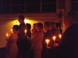 People holding lit candles in a dimly lit indoor gathering