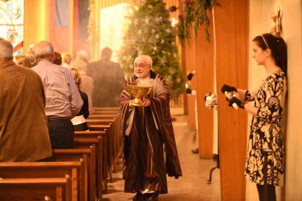 People in a warmly lit church aisle, with a woman holding a camera beside the pews.