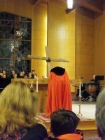 Person in red robe standing at a church altar, facing a congregation in a warmly lit hall