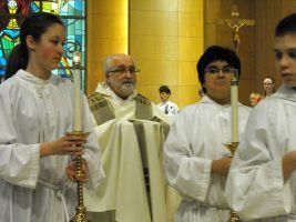 Clergy in white robes processing indoors, carrying tall candles and a ceremonial staff