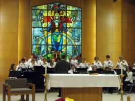 Choir in white robes performing in a church before a colorful stained-glass window