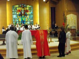 Clergy and choir stand in a church sanctuary before a colorful stained-glass altar.