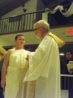 Person in white robe speaking with an older man in white robe at a stage event.