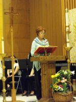 Woman speaking at a church lectern beside a cross and flowers