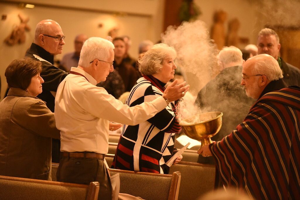 People gathered indoors around a smoking bowl, clapping in a warm-lit room.