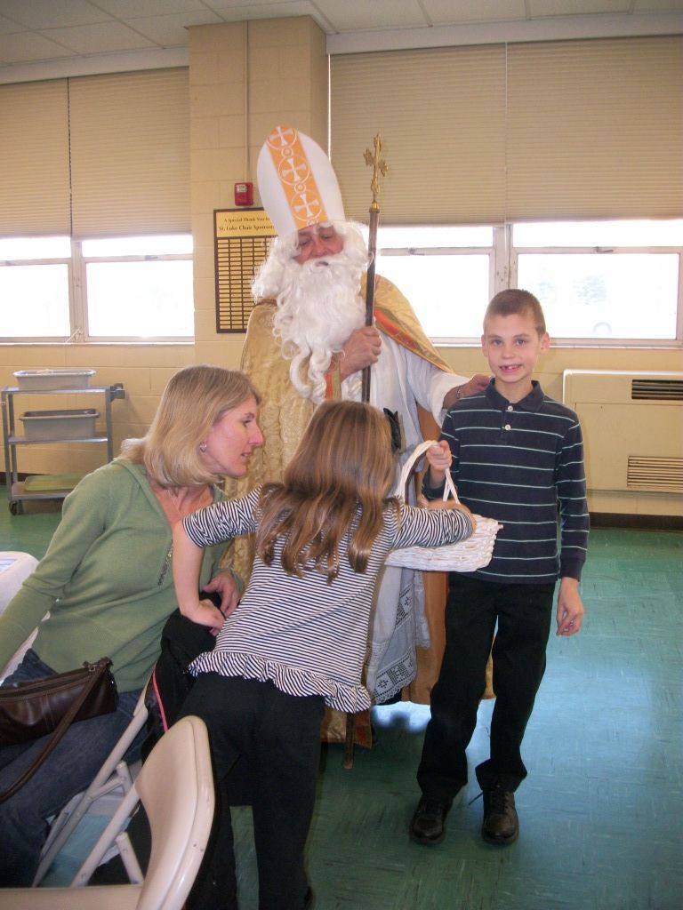 Costumed person with white beard and bishop hat greeting children in a classroom