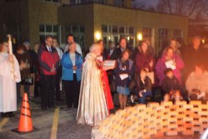 People gathered outdoors at night beside a glowing candle display and an orange traffic cone.