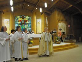 Priests in white robes standing at the altar during a church service, with stained glass in the background