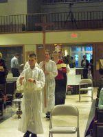 White-robed people walking through a hall with chairs and a balcony in the background.